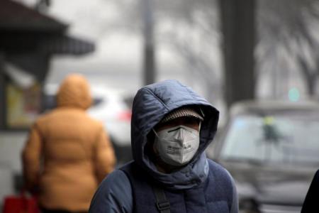 A woman wearing a mask walks along a street during smog on a polluted day in Beijing, China, January 5, 2017. 
