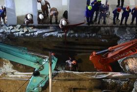 Malaysia Fire and Rescue Department officers inspect the site where a woman fell into an 8m-deep sinkhole in Kuala Lumpur.