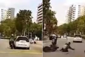 In a video posted on Facebook, a white car is seen hitting a motorcycle as it passes, causing the motorcyclist to fall off.