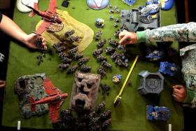 BATTLE FIELD: Players taking turns to move their troops across a large table set up to resemble a war-torn landscape. 