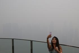 A woman takes a selfie with the skyline of the central business district shrouded by haze in Singapore on Sept 14.