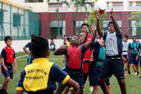 HAVING FUN: Students from Anderson Primary playing a friendly game of Tag 7s, guided by former Singapore player Ong Kim Siang (background). 