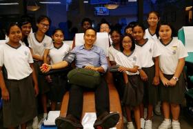 AWARDED: Mr Koh Wee Jin Algene donating blood while primary school pupils look on. 