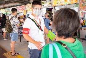 NEA enforcement officer Khong Chee Teck speaking with patrons about safe distancing in a hawker centre.