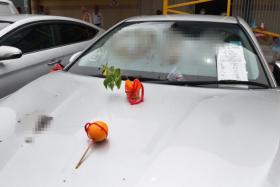 A cake with a flower stuck in it as well as an orange with a red string and two joss sticks were also on the car's bonnet.