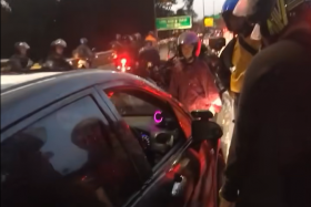 Motorcyclists seen crowding around the car in heavy traffic.