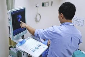 Dr Tan Yu Guang using an ultrasound scan to show patient Tony Wong (not his real name) that the cancer in his bladder is gone.