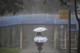 A woman riding an e-scooter with a child while holding an umbrella under the heavy rain next to Block 846 Tampines Street 82 at 8.46am on Oct 14.